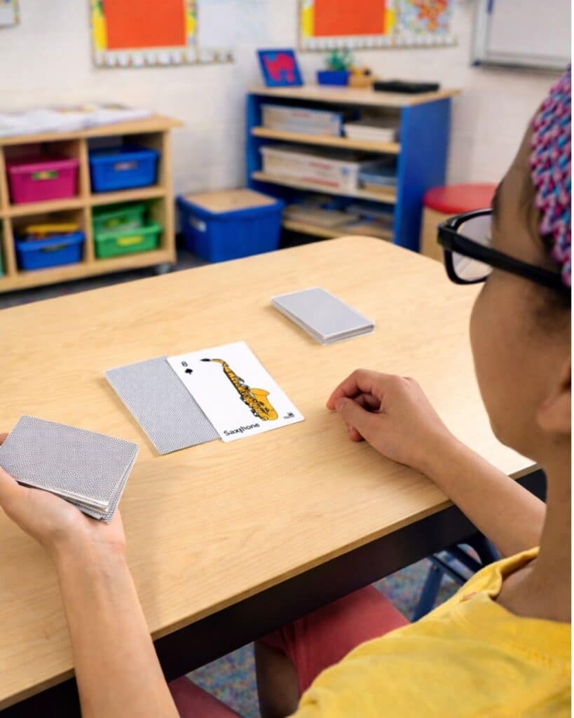 Girl playing a musical instrument card game. She is quizzing her partner (off screen)
